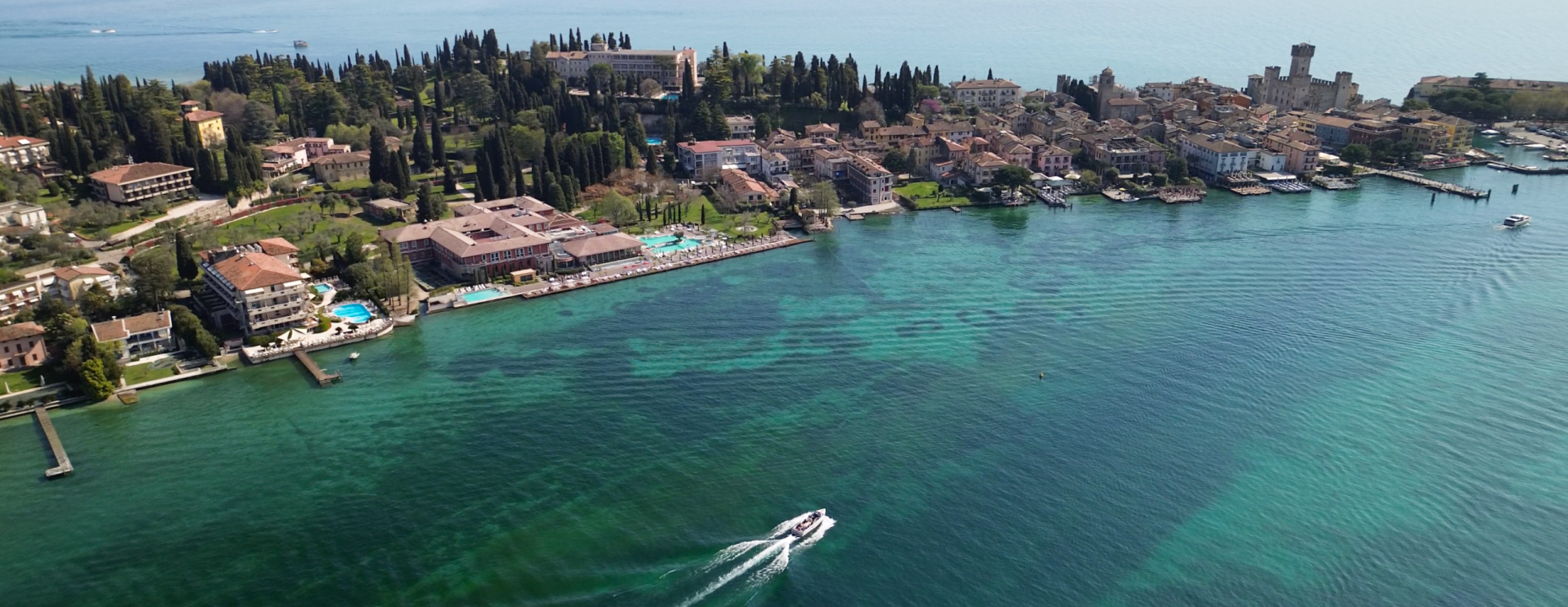 Vista aerea di un pittoresco borgo sul lago, con acque cristalline e barche.
