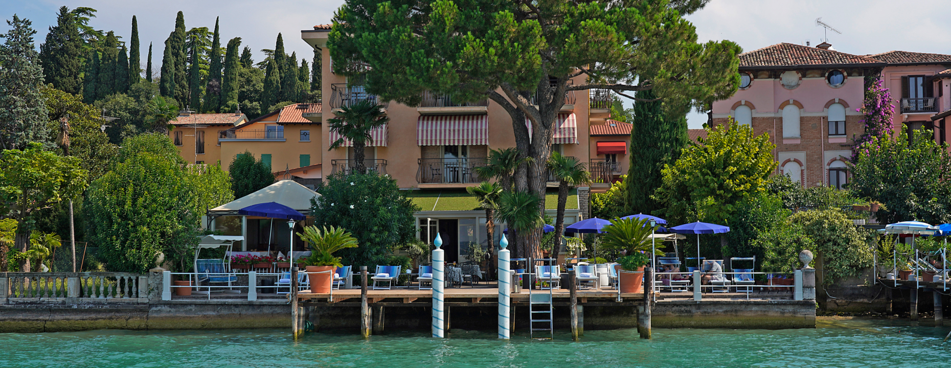 Vista di una villa sul lago con giardino e ombrelloni blu.
